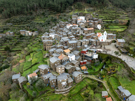 Aerial view of the historical village nestled within terraced hillsides with a prominent white church standing out against the dark stone buildings Piódão Arganil Portugal. Aerial view of the historical village nestled within terraced hillsides with a prominent white church standing out against the dark stone buildings Piódão Arganil Portugal.