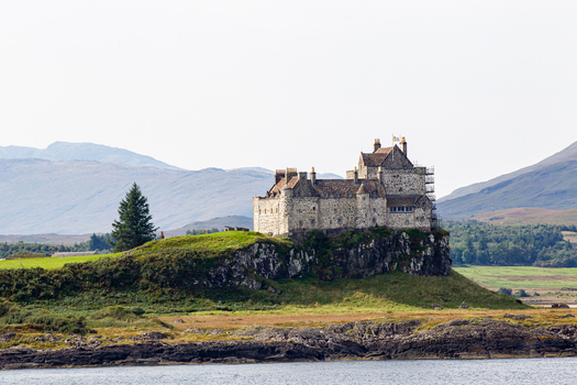 View of Duart Castle standing on a rocky cliff overlooking the water with mountains in the background Isle of Mull Scotland United Kingdom.