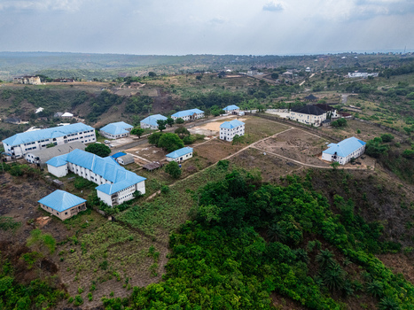 Aerial view of buildings with blue roofs nestled amidst rolling hills and lush greenery a blend of structures and nature Ohafia Abia Nigeria. Aerial view of buildings with blue roofs nestled amidst rolling hills and lush greenery a blend of structures and nature Ohafia Abia Nigeria.