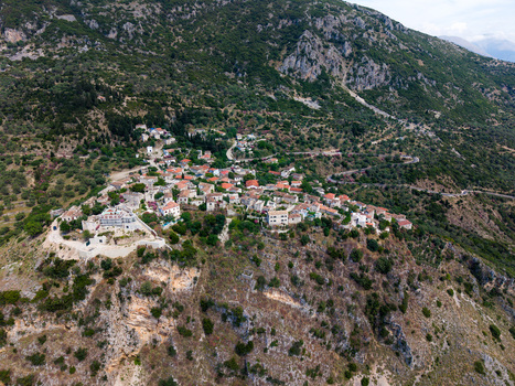 Aerial view of the traditional stone houses and red rooftops of the historic village nestled on a lush green hillside in Qeparo Fshat Vlore County Albania. Aerial view of the traditional stone houses and red rooftops of the historic village nestled on a lush green hillside in Qeparo Fshat Vlore County Albania.