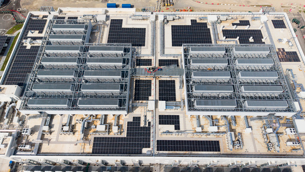 Aerial view of a modern data center campus featuring extensive rooftop solar panel arrays and industrial cooling infrastructure in Melegnano Lombardy Italy.