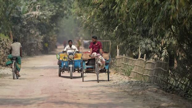 View of people riding rickshaws on a dusty rural road Bangladesh.