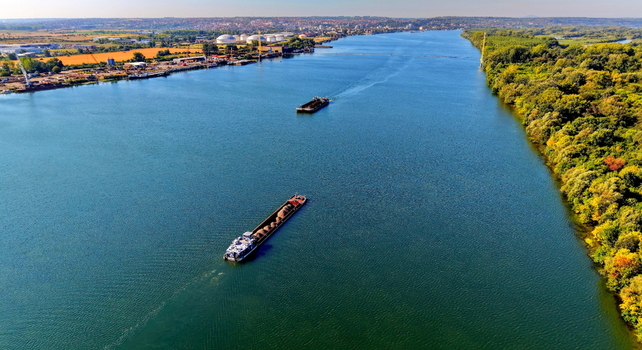 Aerial view of the Danube river with cargo barges navigating past the Smederevo shipyard and industrial facilities along the lush green riverbanks in Smederevo Podunavlje District Serbia. Aerial view of the Danube river with cargo barges navigating past the Smederevo shipyard and industrial facilities along the lush green riverbanks in Smederevo Podunavlje District Serbia.