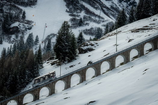View of a vintage train ascends a snow laden mountain on an arched stone railway a stark contrast to the dark evergreens Murren Switzerland. View of a vintage train ascends a snow laden mountain on an arched stone railway a stark contrast to the dark evergreens Murren Switzerland.