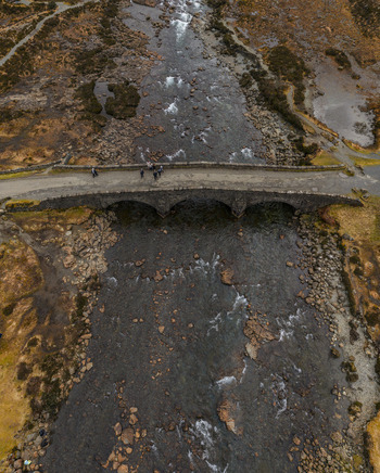 Aerial view of Sligachan Old Bridge spanning a rocky river with people walking across the stone arches in Sligachan Scotland United Kingdom. Aerial view of Sligachan Old Bridge spanning a rocky river with people walking across the stone arches in Sligachan Scotland United Kingdom.