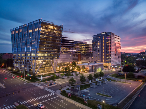 Reston Virginia United States 27 May 2020 Aerial view of modern office buildings and residential towers at twilight with illuminated windows street lights and a parking lot in the foreground. Reston Virginia United States 27 May 2020 Aerial view of modern office buildings and residential towers at twilight with illuminated windows street lights and a parking lot in the foreground.