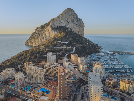 Aerial view of the Penyal d Ifac rock formation towering over the coastal town featuring high rise apartments and a marina filled with boats in Calp Valencian Community Spain. Aerial view of the Penyal d Ifac rock formation towering over the coastal town featuring high rise apartments and a marina filled with boats in Calp Valencian Community Spain.
