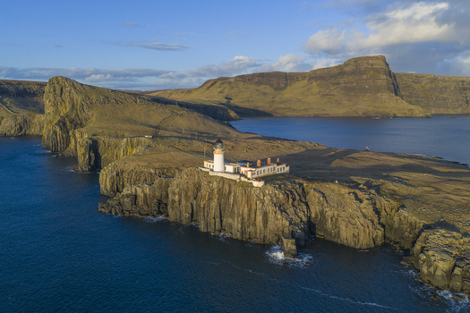 Aerial view of the white Neist Point Lighthouse situated on the edge of steep dark cliffs overlooking the blue sea in Isle of Skye Scotland United Kingdom. Aerial view of the white Neist Point Lighthouse situated on the edge of steep dark cliffs overlooking the blue sea in Isle of Skye Scotland United Kingdom.
