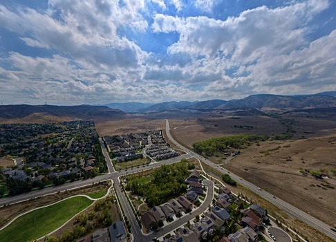 Aerial view of a suburban neighborhood with modern houses winding roads and green spaces set against the backdrop of the rolling foothills in Golden Colorado United States.