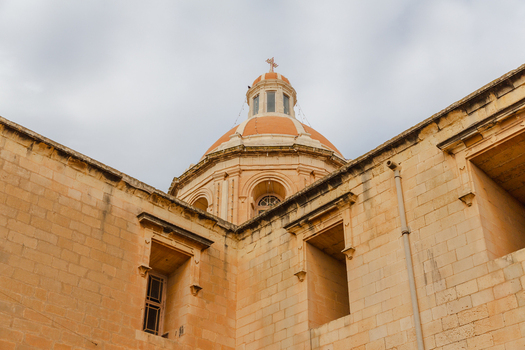 View of the striking dome of the Parish Church casting a warm glow against the cloudy sky a beacon of faith and architecture Marsaxlokk Malta. View of the striking dome of the Parish Church casting a warm glow against the cloudy sky a beacon of faith and architecture Marsaxlokk Malta.