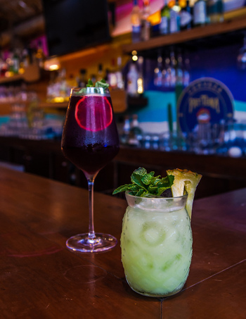 View of two refreshing cocktails a dark red drink and a light green drink with mint and pineapple on a wooden bar counter San Jose del Cabo Baja California Sur Mexico.