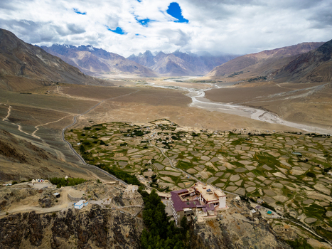Aerial view of Zanskar monastery in the rugged valley surrounded by green terraced fields a winding river and dramatic mountain peaks in Zanskar Ladakh India.