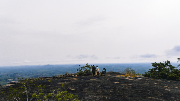 Aerial view of dark rocky terrain meets a distant horizon under a vast pale sky with figures standing atop Oyo Oyo Nigeria. Aerial view of dark rocky terrain meets a distant horizon under a vast pale sky with figures standing atop Oyo Oyo Nigeria.