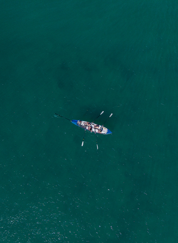 Aerial view of a rowing boat with people rowing on the turquoise waters of the ocean off the coast of Dee Why New South Wales Australia. Aerial view of a rowing boat with people rowing on the turquoise waters of the ocean off the coast of Dee Why New South Wales Australia.