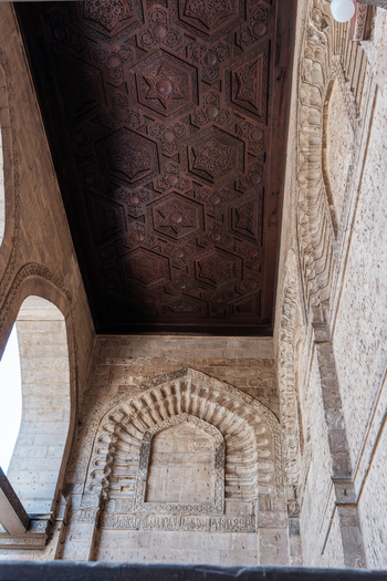View of the Mosque of al Salih Tala i featuring an intricate carved wooden ceiling with geometric star patterns and stone arched niches in Cairo Egypt. View of the Mosque of al Salih Tala i featuring an intricate carved wooden ceiling with geometric star patterns and stone arched niches in Cairo Egypt.
