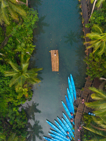 Aerial view of the Maasin River with a wooden raft floating in the water blue boats moored at a wooden dock and lush coconut palm trees along the riverbanks in Siargao Philippines. Aerial view of the Maasin River with a wooden raft floating in the water blue boats moored at a wooden dock and lush coconut palm trees along the riverbanks in Siargao Philippines.