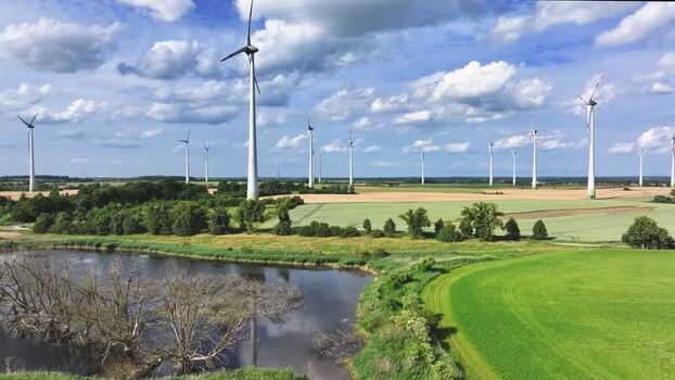 Aerial view of wind turbines over rural fields and a pond Germany.