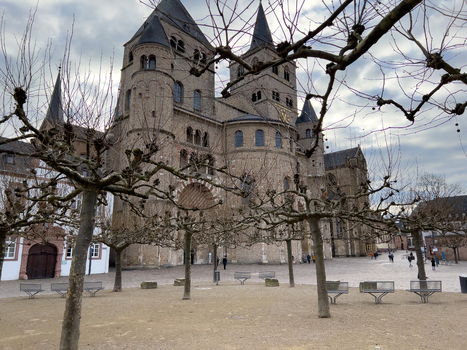 View of Trier Cathedral with its historic stone facade arched doorways and bare trees in the foreground under a cloudy sky in Trier Rheinland Pfalz Germany.