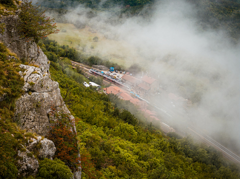 Aerial view of a train station nestled in a valley surrounded by lush green hills and rocky cliffs partially obscured by low hanging clouds in Buzet Istria County Croatia.