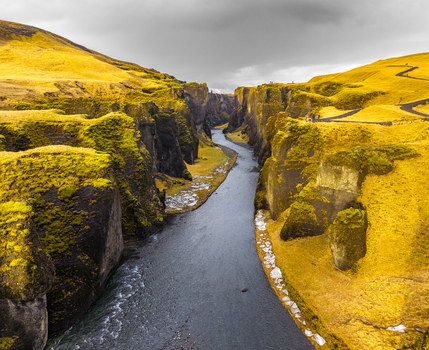 Aerial view of the dark river snaking through the golden canyon under a moody sky Fjaðrárgljúfur Iceland. Aerial view of the dark river snaking through the golden canyon under a moody sky Fjaðrárgljúfur Iceland.