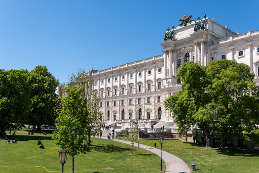 View of the historic Neue Burg wing of the Hofburg Palace with people relaxing on the green lawn of the Burggarten under a clear blue sky in Vienna Vienna Austria. View of the historic Neue Burg wing of the Hofburg Palace with people relaxing on the green lawn of the Burggarten under a clear blue sky in Vienna Vienna Austria.