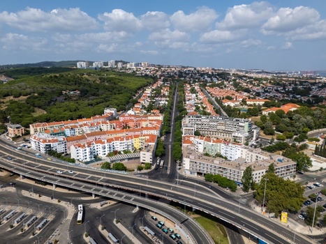 Aerial view of the town of Alges featuring residential buildings a major highway interchange and surrounding green areas in Alges Lisbon Portugal.