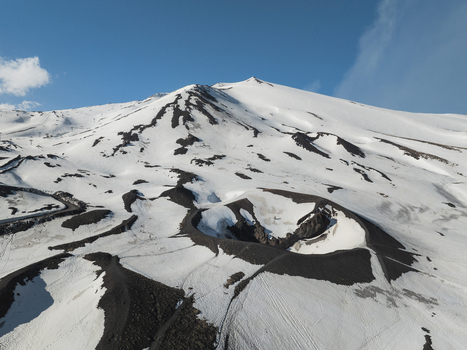 Aerial view of the snow covered southern slope of Mount Etna featuring a volcanic crater and the majestic peak under a clear blue sky in Nicolosi Sicilia Italy. Aerial view of the snow covered southern slope of Mount Etna featuring a volcanic crater and the majestic peak under a clear blue sky in Nicolosi Sicilia Italy.