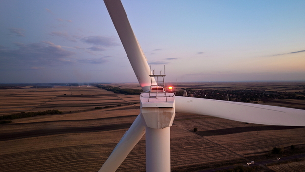 Aerial view of a wind turbine at sunset with a red warning light overlooking the vast agricultural fields of the Pannonian Basin in Vladimirovac Vojvodina Serbia. Aerial view of a wind turbine at sunset with a red warning light overlooking the vast agricultural fields of the Pannonian Basin in Vladimirovac Vojvodina Serbia.
