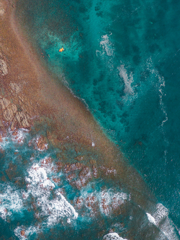 Aerial view of a rocky coastline meeting the turquoise sea with a small orange boat floating in the clear water in Costa Rica.