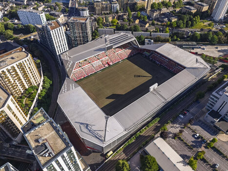 Aerial view of Gtech Community Stadium with its red seating and green pitch surrounded by modern residential buildings and railway tracks in Brentford England United Kingdom. Aerial view of Gtech Community Stadium with its red seating and green pitch surrounded by modern residential buildings and railway tracks in Brentford England United Kingdom.