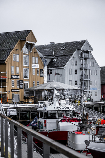 Tromso Norway 07 March 2026 View of traditional wooden harbor buildings and a boat docked at the pier under an overcast sky. Tromso Norway 07 March 2026 View of traditional wooden harbor buildings and a boat docked at the pier under an overcast sky.