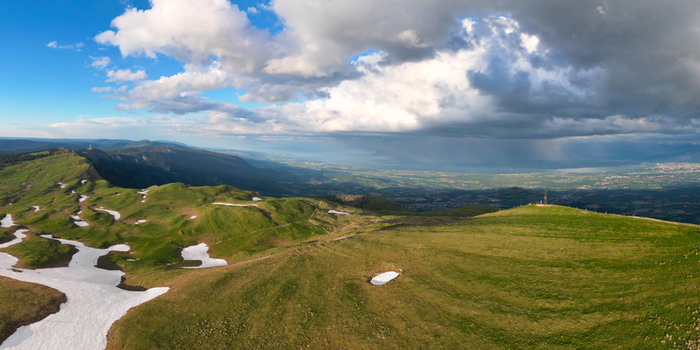 Aerial view of Le Colomby de Gex with green mountain ridges patches of snow and dramatic rain clouds over the valley near Echenevex Auvergne Rhone Alpes France. Aerial view of Le Colomby de Gex with green mountain ridges patches of snow and dramatic rain clouds over the valley near Echenevex Auvergne Rhone Alpes France.