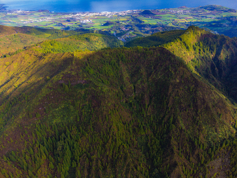 Aerial view of Lagoa do Fogo volcanic mountains covered in dense green forest with the coastal town and ocean in the distance Agua de Alto Azores Portugal. Aerial view of Lagoa do Fogo volcanic mountains covered in dense green forest with the coastal town and ocean in the distance Agua de Alto Azores Portugal.