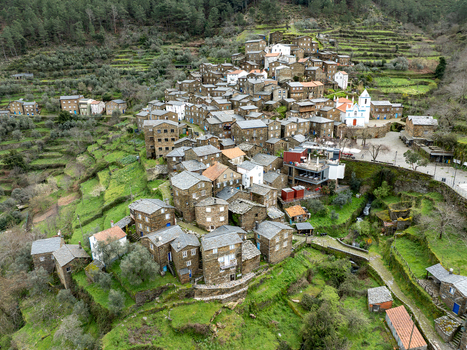 Aerial view of the quaint village nestled among vibrant green terraces with the church standing out in stark white against the dark stone houses Piódão Arganil Portugal. Aerial view of the quaint village nestled among vibrant green terraces with the church standing out in stark white against the dark stone houses Piódão Arganil Portugal.