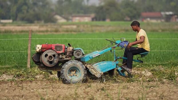 View of a farmer operating a power tiller in a field Nepal. View of a farmer operating a power tiller in a field Nepal.