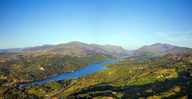 Aerial view of Llyn Padarn lake surrounded by lush green hills rocky mountains and dense forests under a clear blue sky in Cwm y glo Wales United Kingdom. Aerial view of Llyn Padarn lake surrounded by lush green hills rocky mountains and dense forests under a clear blue sky in Cwm y glo Wales United Kingdom.
