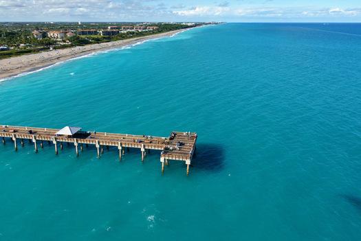 Aerial view of the Juno Beach Pier where the pale wooden structure meets the turquoise ocean contrasting with the golden sands and buildings Juno Beach Florida United States.