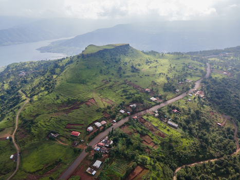 Aerial view of the lush green Kaas plateau with a winding road scattered houses and a lake in the background in Satara Maharashtra India.