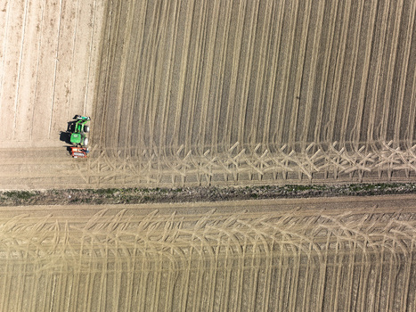 Aerial view of a green tractor working in a tilled agricultural field with geometric furrows and tire tracks in Rivalta di Torino Piedmont Italy. Aerial view of a green tractor working in a tilled agricultural field with geometric furrows and tire tracks in Rivalta di Torino Piedmont Italy.