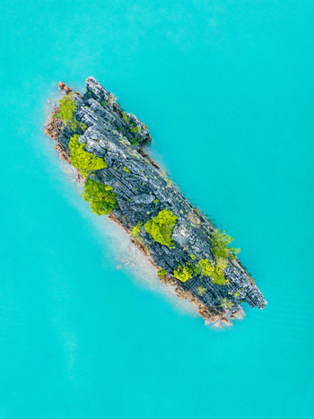 Aerial view of a jagged rocky island with green vegetation surrounded by vibrant turquoise water in Vietnam. Aerial view of a jagged rocky island with green vegetation surrounded by vibrant turquoise water in Vietnam.