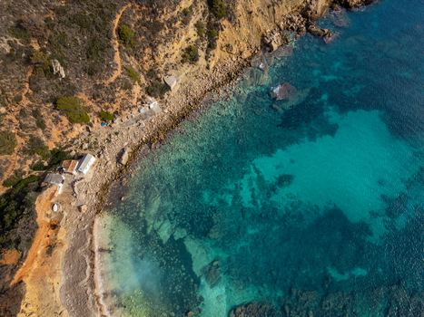 Aerial view of Cala Llebeig with its turquoise waters rocky coastline and small traditional fishermen s huts in El Poble Nou de Benitatxell Valencian Community Spain.