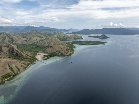 Aerial view of Komodo Island with lush green hills turquoise waters and boats along the coastline in Komodo East Nusa Tenggara Indonesia. Aerial view of Komodo Island with lush green hills turquoise waters and boats along the coastline in Komodo East Nusa Tenggara Indonesia.