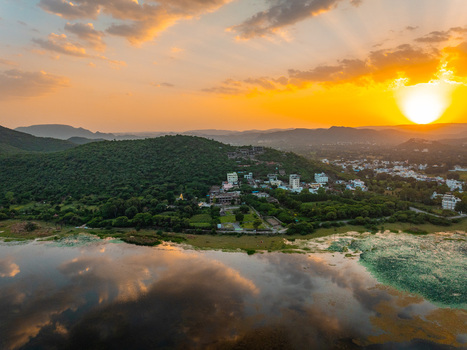 Aerial view of the lush green hills and buildings surrounding a tranquil lake in Udaipur during a vibrant golden sunset Udaipur Rajasthan India.