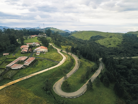 Aerial view of a winding road snaking through verdant hills towards buildings with warm orange roofs Obudu Cross River Nigeria.
