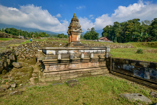 View of the ancient stone temple at Situs Liyangan surrounded by stone walls and lush greenery under a blue sky in Ngadirejo Central Java Indonesia.