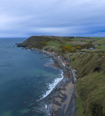 Aerial view of the historic fishing village nestled at the base of steep green cliffs along the rocky coastline of the North Sea in Crovie Scotland United Kingdom.