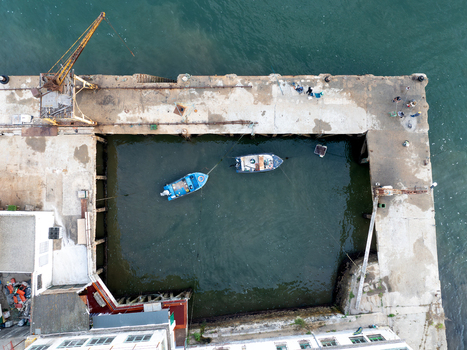 Aerial view of Ginjal Pier with small blue boats moored in the basin featuring an old yellow crane and people on the concrete dock Almada Setubal Portugal. Aerial view of Ginjal Pier with small blue boats moored in the basin featuring an old yellow crane and people on the concrete dock Almada Setubal Portugal.