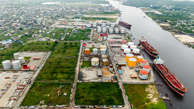Aerial view of the industrial port area in Satellite Town featuring large oil storage tanks cargo ships docked along the river and trucks parked in the facility in Lagos Lagos Nigeria.