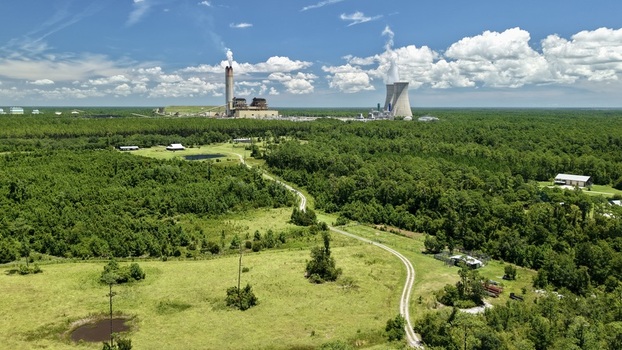 Aerial view of Seminole Generating Station with its cooling towers and smokestack rising above the surrounding lush green forest and rural landscape in Palatka Florida United States.