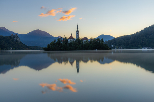 View of Lake Bled with the Pilgrimage Church of the Assumption of Maria on the island reflected in the calm water at sunrise with mountains in the background Bled Radovljica Slovenia.